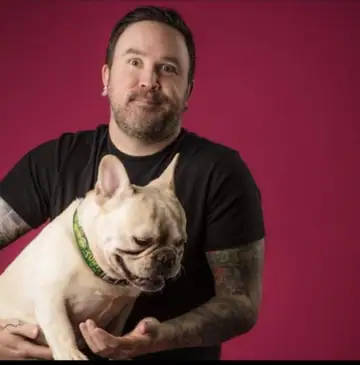 Raymond in a black T-shirt against a magenta backdrop, holding a fawn French bulldog, Long Beach dog walker